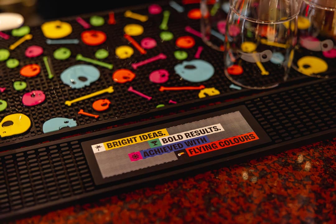 A black bar runner on a bar with colourful branding and the words "Bright Ideas, Bold Results, Achieved with Flying Colors."