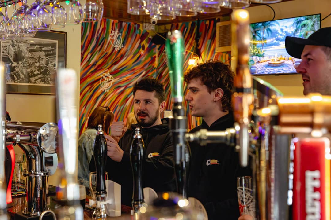 A shot through a bar of two guys wearing blackToucan International hoodies ordering beers.