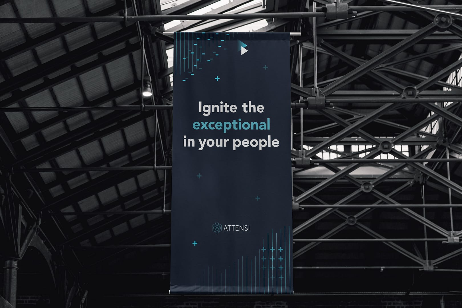 vertical banner hanging in an industrial setting, with "Ignite the exceptional in your people" in large letters, alongside blue digital graphic and the Attensi logo.