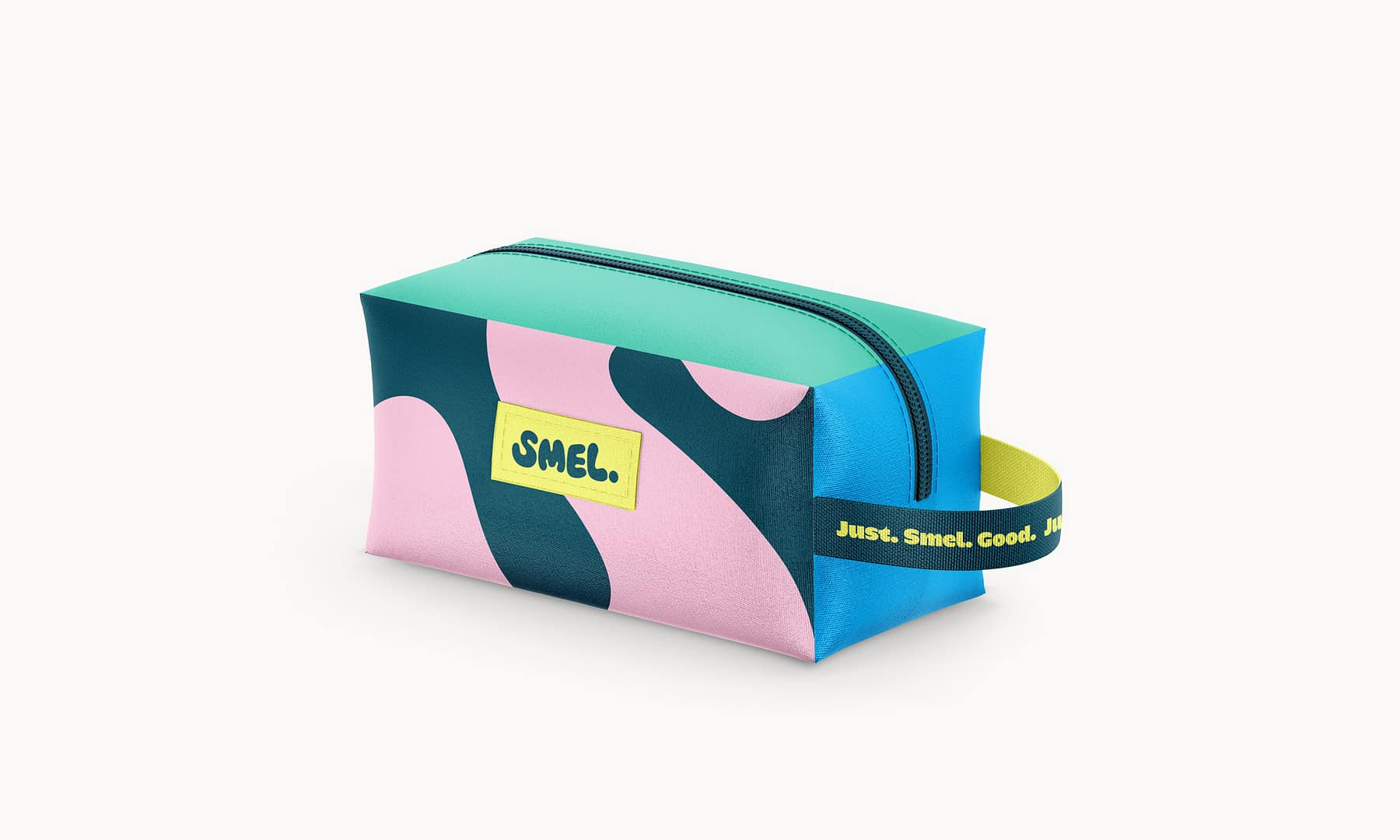 Colourful SMEL washbag with an abstract teal, pink, and blue pattern, set against a light background. The bag features a bright yellow SMEL logo patch and a dark teal handle strap printed with "Just. Smel. Good." in yellow text.
