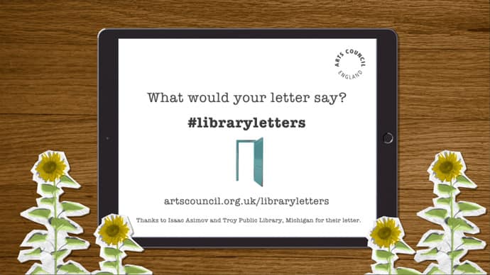 Animation still showing an iPad on a wooden desk surrounded by cutout paper sunflowers. On the iPad is the Arts Council England logo and text which reads “What would your letter say?” Along with the hashtag #libraryletters and the web address artscouncil.org.uk/libraryletters